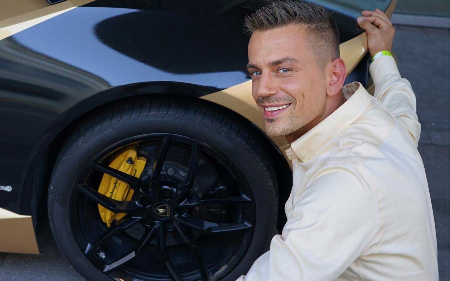 Ein lächelnder Mann prüft neben einem Luxusauto mit schwarzen Felgen und gelben Bremssätteln.