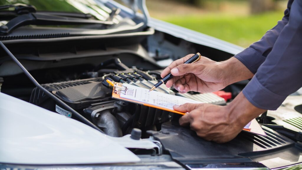 Ein Mann steht vor einer offenen Motorhaupe eines Autos mit einer Checkliste in en Händen.