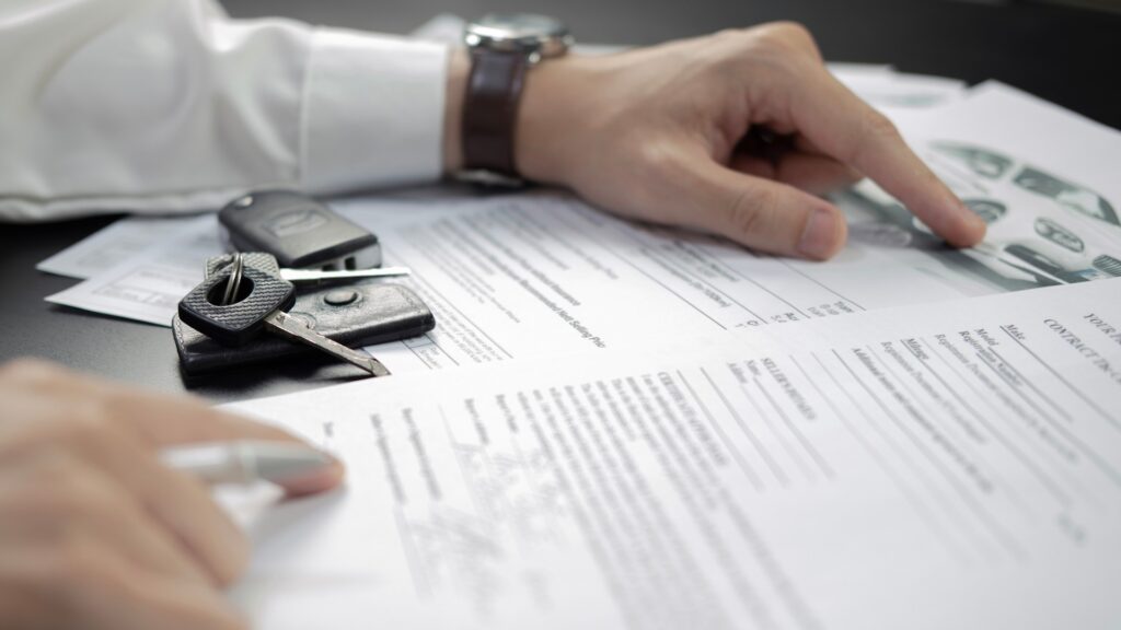 Eine Person prüft Autopapiere. Ein Zündschlüssel liegt auf den Papieren.
